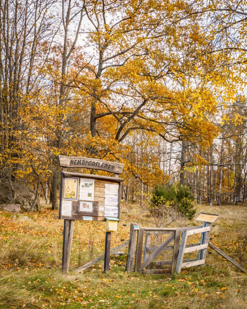 Informationstavla med texten "Hembygdsleden" vid starten av Landeryds hembygdsled, omgiven av höstfärgade träd och en trädgrind.