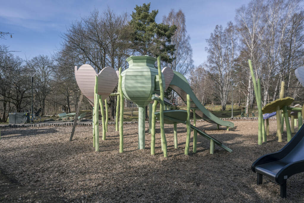 Kreativ lekplats i Magistratshagen, Ekkällan, med fantasifulla klätterställningar formade som gröna insekter och rutschkana bland björkar.