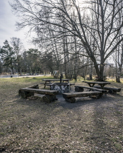 Grillplats med rustika stockbänkar och grillring i Magisterhagen, Linköping, omgiven av lövträd på tidig vår.