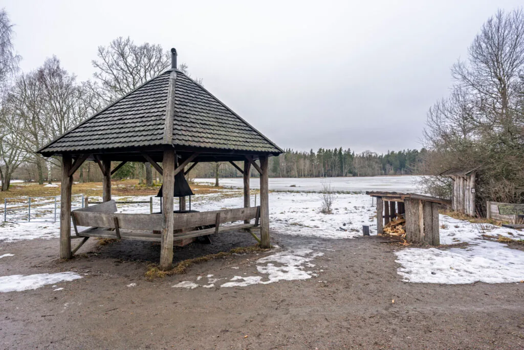 Grillpaviljong med bänkar i Ekängsdalen vid snötäckt våtmark, en mulen vinterdag längs Östgötaleden i Linköpings kommun