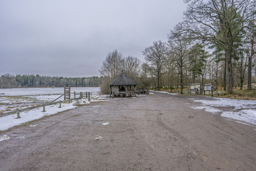 Rastplats vid Ekängs parkering med vindskydd, grillplats och informationsskyltar vid snötäckt våtmark i Ekängsdalen, Linköping Under gråmulen vinterdag.