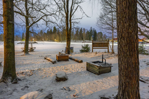 Snötäckt grillplats vid Vallamasivet i Linköping med eldstad, sittplatser och kala träd i vinterskymning