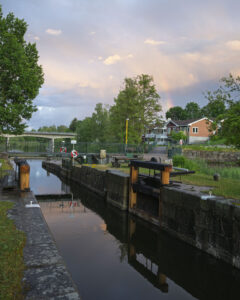 Hjulsbro sluss längs Stångåstråket i Linköping en sommarkväll med regnbåge, slussportar, livbojar och hus i bakgrunden