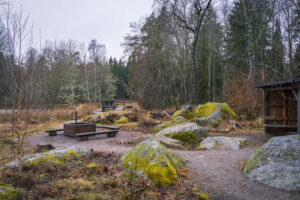 Rastplats vid Ullabergs våtmark med grillplats, mossbeklädda stenblock och vindskydd omgivna av björk- och barrskog en grå vinterdag