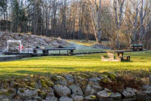 Slattefors sluss vid Kinda kanal en tidig vårmorgon med frostigt gräs, slussluckor, skylt och rastplats med bänkbord omgivna av lövträd.