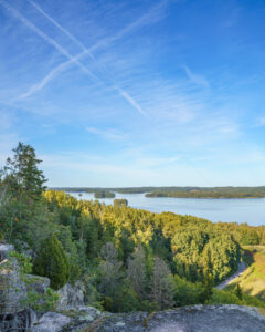 Utsikt från Klevberget över Ärlången med skogsklädda stränder och små öar, en solig dag i Kinda kommun, Östergötland