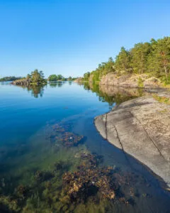 Klippor och stilla vatten vid Eköns naturreservat i Gryts skärgård, med slätslipade hällar, tång och tallbevuxna öar en sommardag