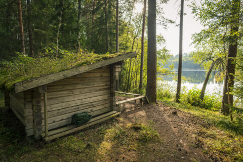 Vindskydd i timmer med mossbeklätt tak vid sjön Drien, omgivet av skog längs Östgötaleden mellan Smedstorp och Pinnarp