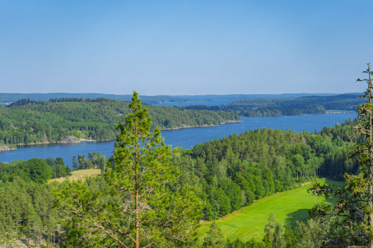 Utsikt från Hisneklint över Kinda kanal, omgiven av grön barrskog och ängar i Östergötland.