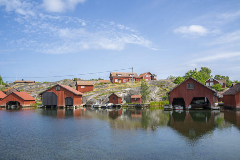 Röda sjöbodar och båthus vid vattnet på Harstena i Gryts skärgård, med klippor och faluröda stugor i bakgrunden