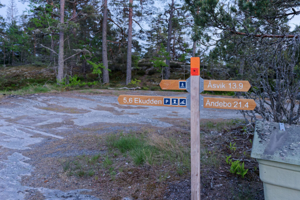 Vägvisare längs Östgötaleden med skyltar mot Åsvik, Ändebo och Ekudden på klipphäll i skogsmiljö.