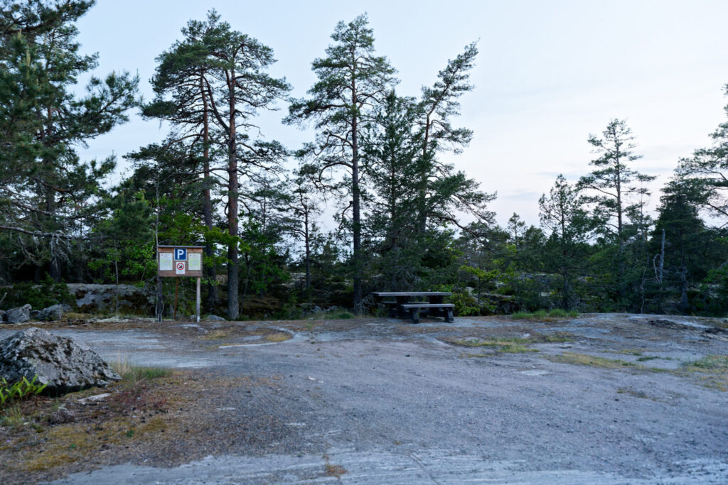 Parkeringsplats med informationstavla och picknickbord bland tallar vid Kvädöfjärdens fågeltorn.