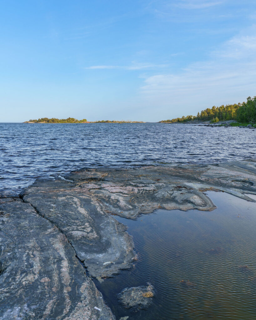 Slipade klipphällar vid vattenbrynet längs Ekuddeslingan i Valdemarsviks skärgård, med skogklädda öar i horisonten.