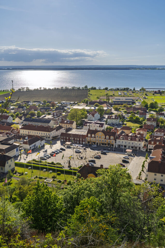 Utsikt över Gränna torg med färgglada handelshus och Vättern glittrande i bakgrunden på en solig dag.