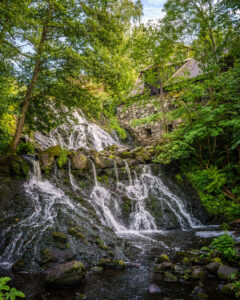 Röttle vattenfall omgivet av frodig grönska med Jerusalems kvarn på klippan ovanför, längs Röttlestigen i Småland