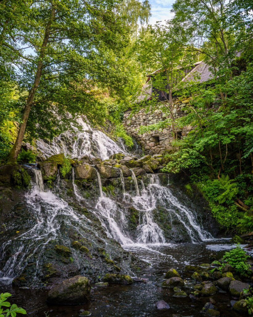 Röttle vattenfall omgivet av frodig grönska med Jerusalems kvarn på klippan ovanför, längs Röttlestigen i Småland