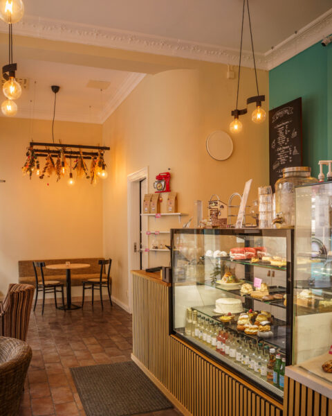Mysig interiör på Petra's Cake, Pastry & café i Linköping med glasdisk fylld av tårtor och bakverk, hängande lampor med torkade blommor och sittplatser i varma toner.