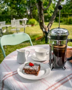 Fika med chokladkaka och presskaffe på ett trädgårdsbord i grönskan vid Kafé Skedet nära Omberg, Vadstena kommun