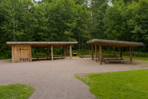 Öppna vindskydd med bänkbord och grillplats vid Östanåparken i Tranås, omgivna av lummig lövskog.