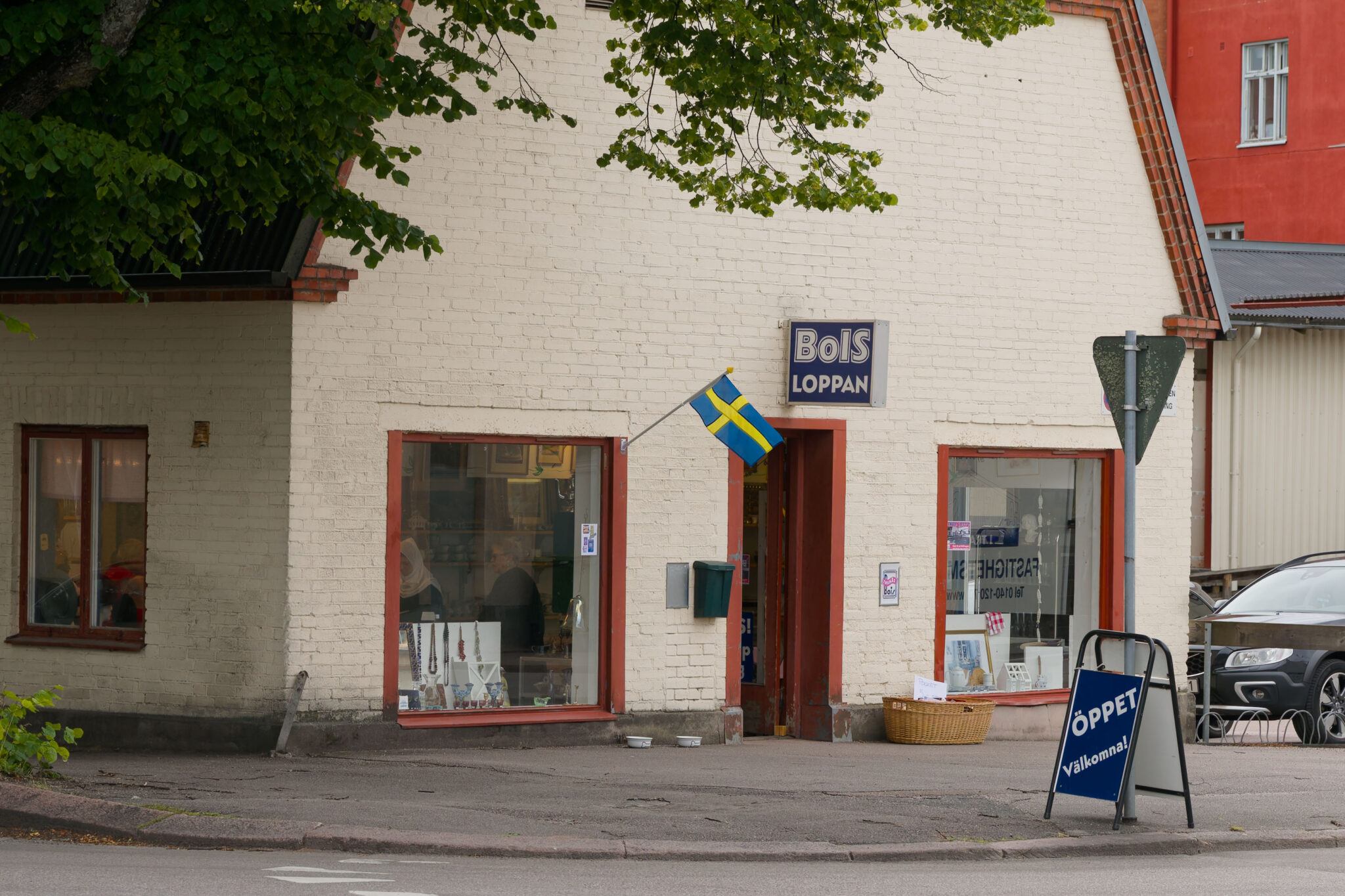 Loppisen BoIS-loppan i Tranås, ett vitt tegelhus med svensk flagga och skylt med texten "Öppet – Välkommen!"