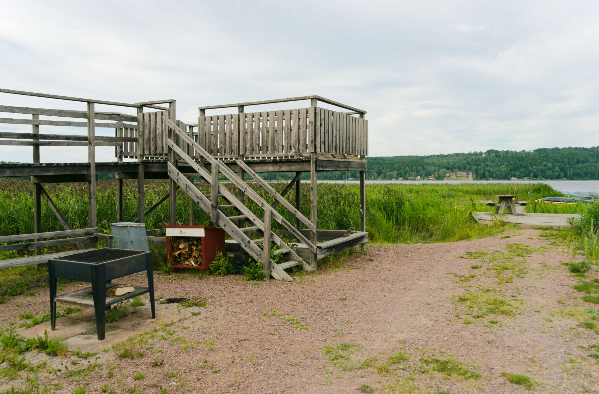 Träplattform med trappa vid Säbysjön i Tranås, omgiven av vass och grönskande strandäng med sjö och skog i bakgrunden.