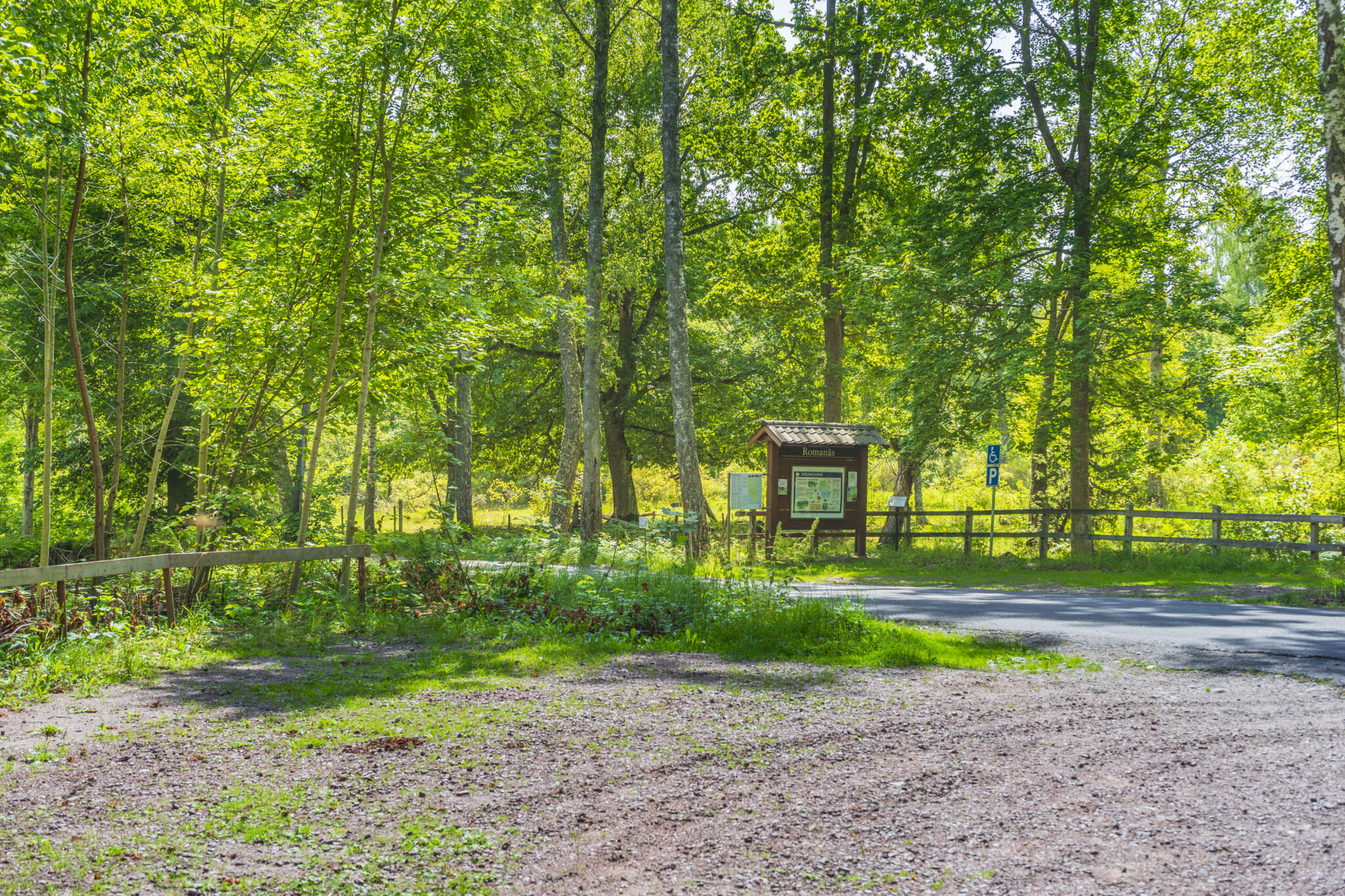 Informationsskylt och grusad parkeringsplats vid naturreservat omgivet av lövskog i Romanäs, Tranås kommun.