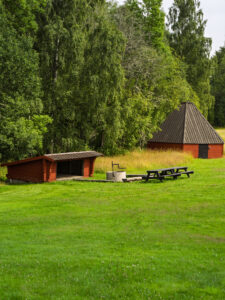 Rastplats med rödmålad grillkota, vindskydd och picknickmöbler på grönskande gräsmatta vid sjön Illern i Tranås kommun.