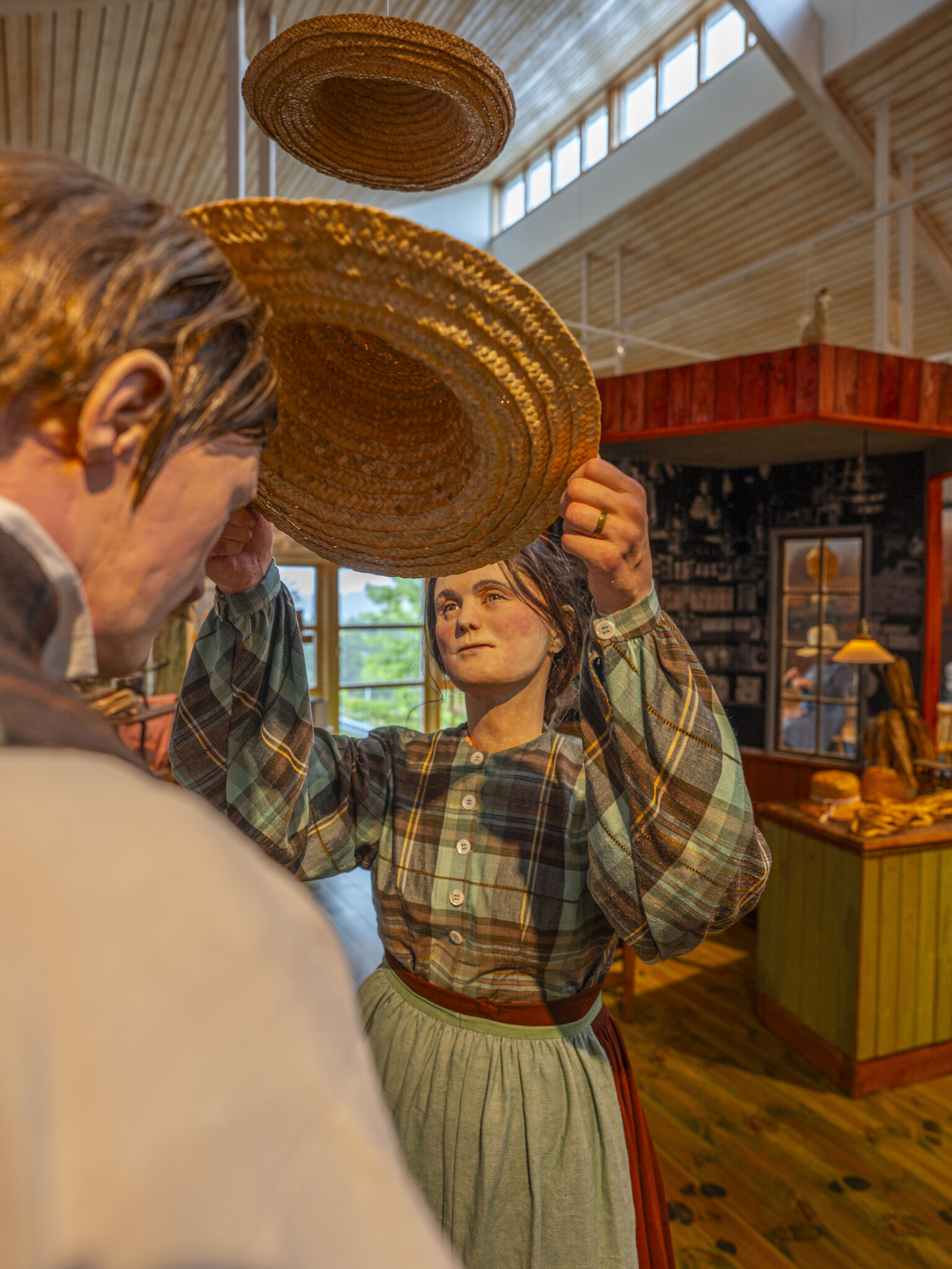 Vaxfigurer i historiska kläder håller upp halmhattar inne på Halmens Hus i Bengtsfors, Dalsland.