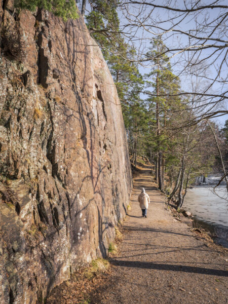 Person promenerar på stig längs en brant klippvägg vid isbelagd sjö i skogen vid Ågelsjön, Norrköping.