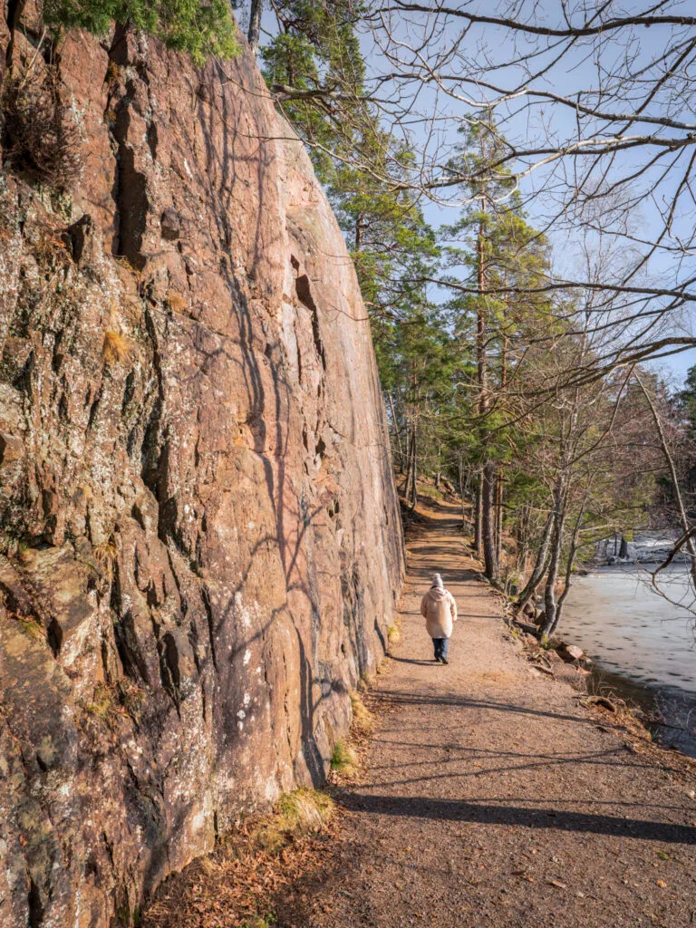 Person promenerar på stig längs en brant klippvägg vid isbelagd sjö i skogen vid Ågelsjön, Norrköping.