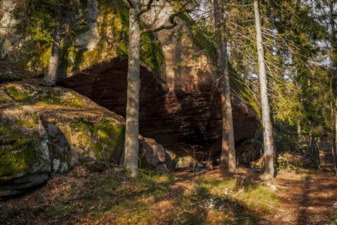 Stor klippa med mossbelupna stenar bildar ett naturligt vindskydd i skogen vid Eremitgrottan nära Jakobsdal, Norrköping.