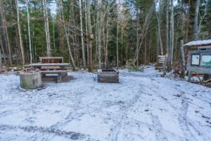 Snötäckt grillplats med eldstad, picknicbord och informationsskylt vid Säby Västerskog i vinterskrud.