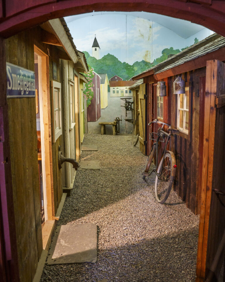 Museiutställning på Melleruds museum med rekonstruerad gränd vid Smedjegatan, gammalt trähus och cykel mot väggen.