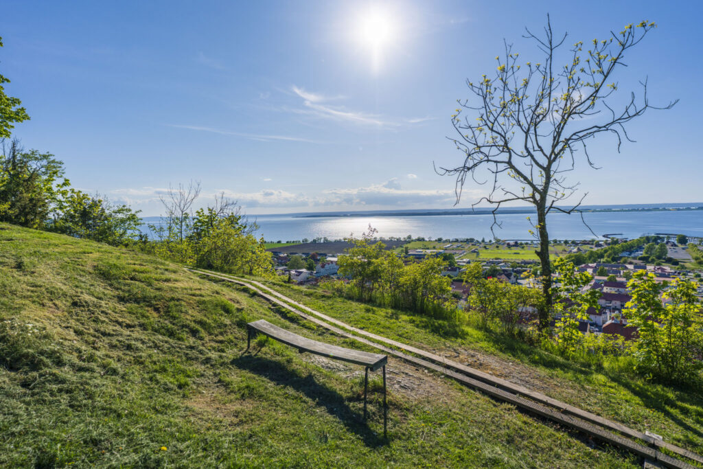 Utsikt från Grännaberget ovanför Trolltrappan med bänk, grönska och Vättern i bakgrunden en solig sommardag.