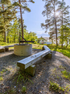 Eldplats med träbänkar och grillgaller vid Oscarshöjd i Gränna, med ett vitt lusthus och tallskog i bakgrunden.