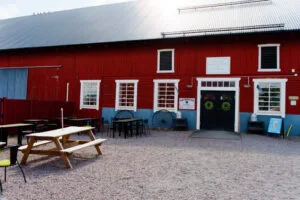 Röd lada med gårdsbutik och uteservering med picknickbord på grusplan vid Åkerbys gårdsbutik och lantcafé i Östergötland.