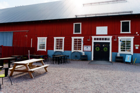 Röd lada med gårdsbutik och uteservering med picknickbord på grusplan vid Åkerbys gårdsbutik och lantcafé i Östergötland.