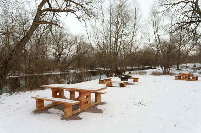Snötäckt rastplats med träbänkbord och grillplats vid Sångans å nära Ullevibron utanför Linköping