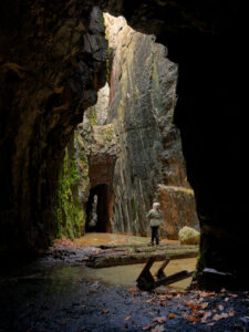 Person står i det imponerande bergrummet i Stenebo gruva vid Ukna, med höga klippväggar, mossa och vattensamlingar på golvet
