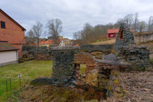 Ruiner av den gamla smedjan och masugnsgrunden i Edsbruk, med stenmurar, tegelbyggnad och herrgårdsmiljö i bakgrunden.